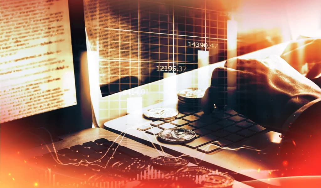 Hands typing on laptop with Bitcoin coins and stock market charts overlaid in blue light.