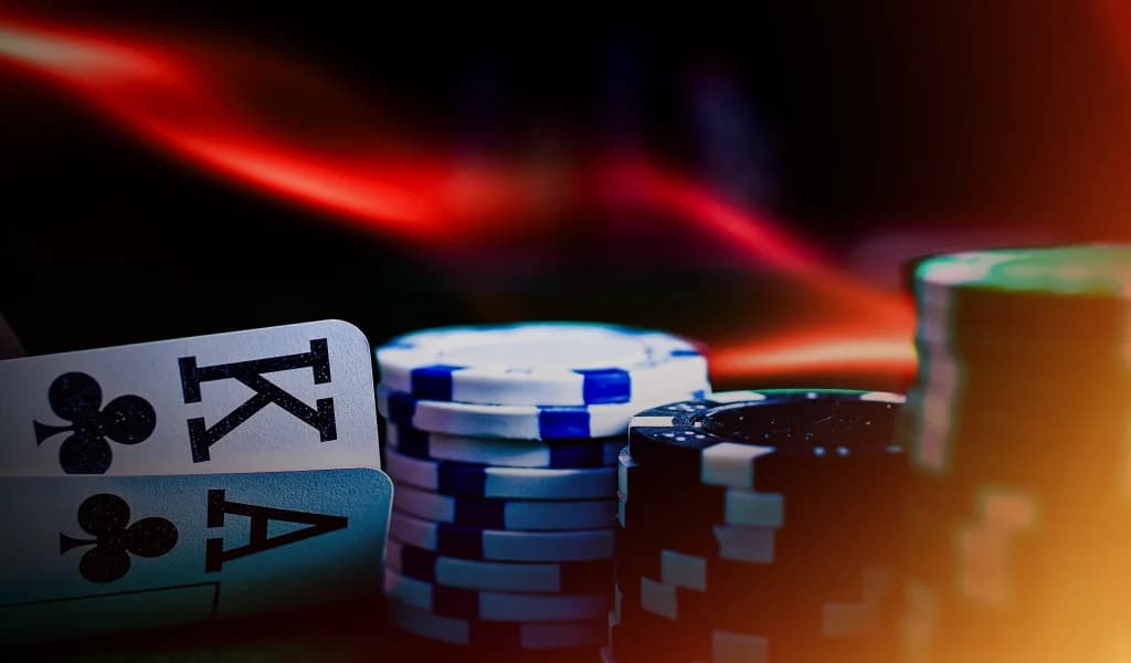 King and ace of clubs beside stacked poker chips on a table with a red and black background.