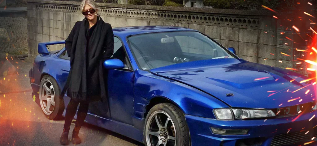 Bridget Burt dressed in an all black outfit leaning up against a blue car.