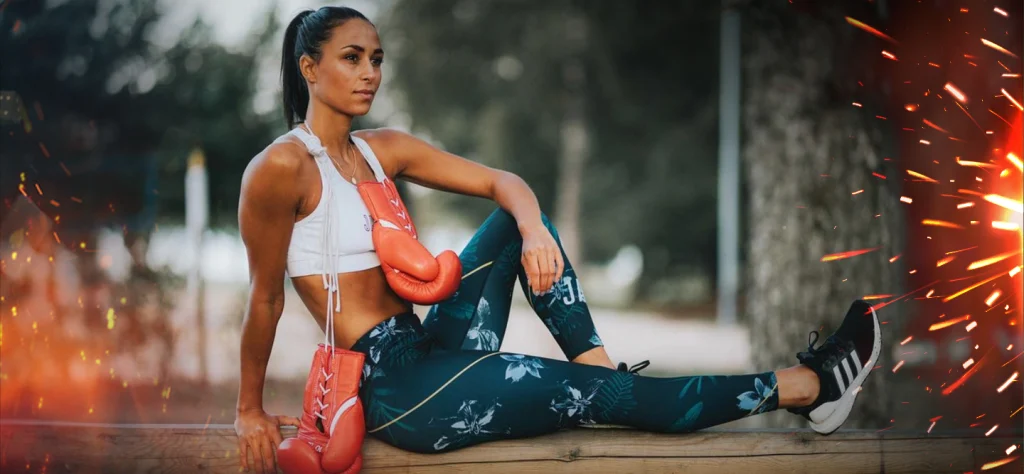 Professional boxer Linn Sandström is sitting on a wall with boxing gloves hanging from her neck.