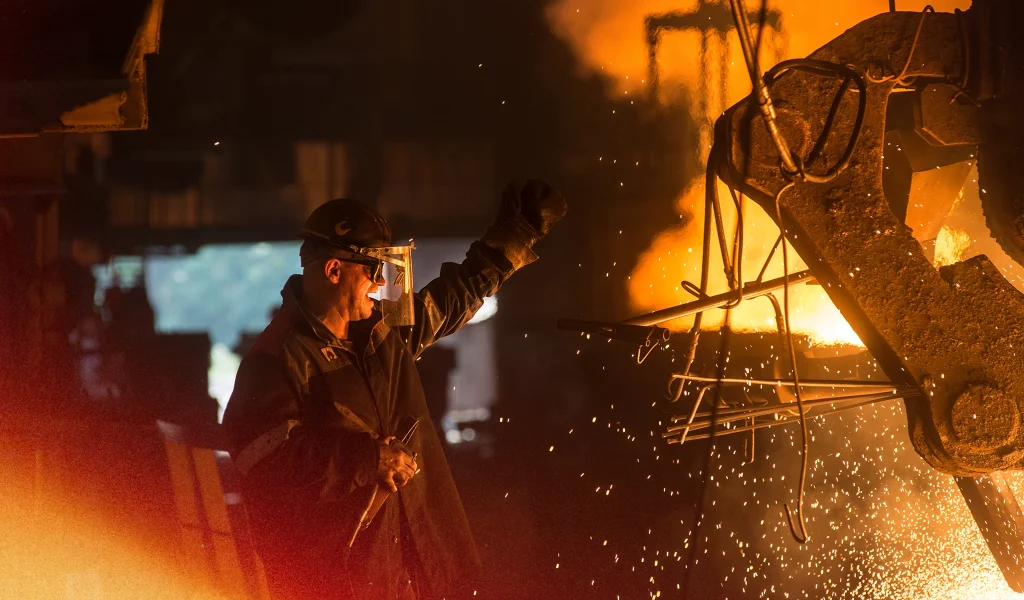 Ironworker wearing protective gear near molten metal sparks flying in a fiery industrial environment.