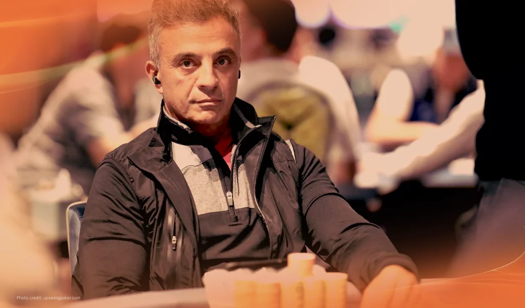 Joe Hachem sits at a poker table, staring ahead with a serious expression, surrounded by stacks of poker chips.