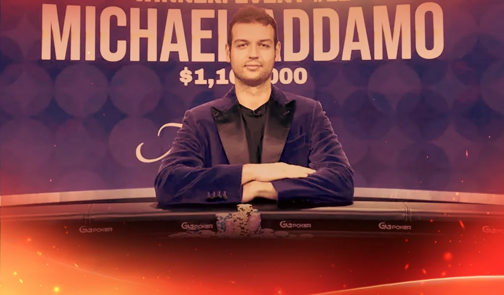 Michael Addamo sits at a poker table with folded arms, chips in front, and his name displayed behind him.