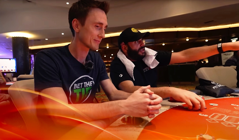 Casino King Matt Gothard sitting at a poker table with another player pointing at the table in a casino.