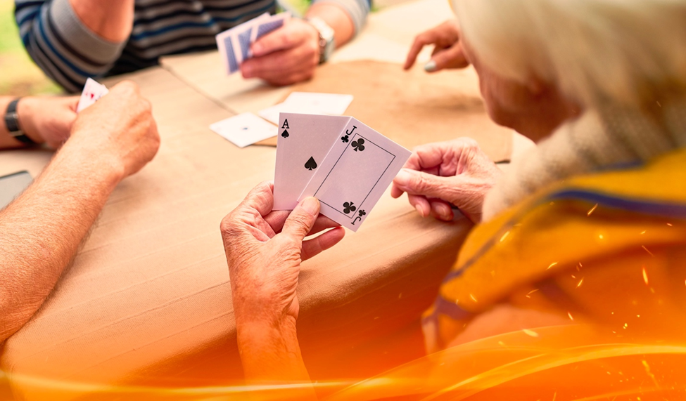 Elderly individuals playing poker at a table, with one person holding an Ace and Jack of clubs.