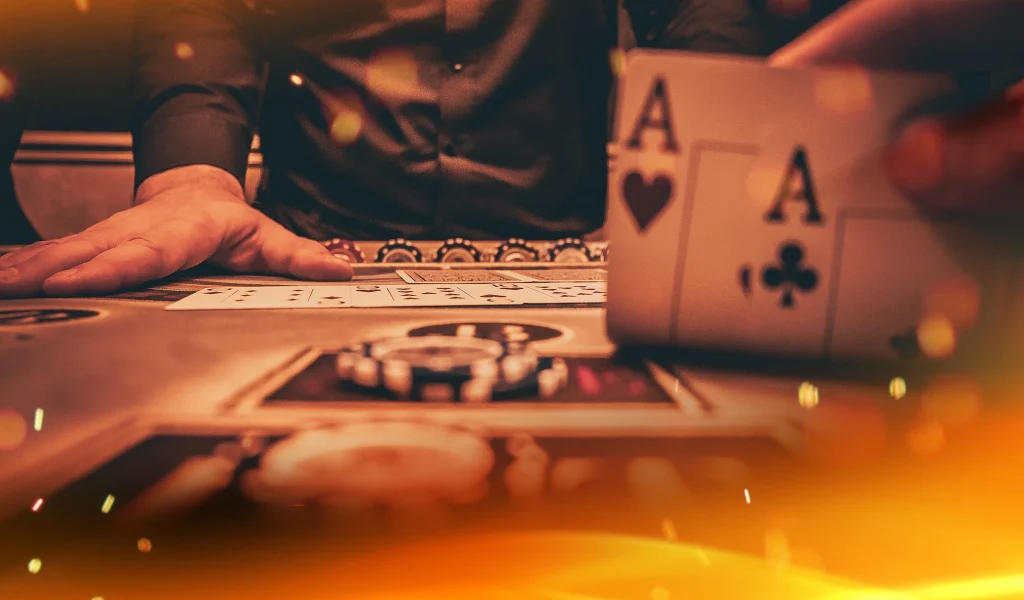 Close-up of a poker table with a player holding pocket aces while another hand rests near the community cards.