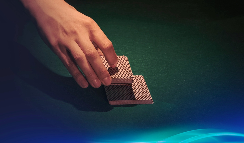 A hand cutting a deck of playing cards on a green felt table, preparing for the next deal.