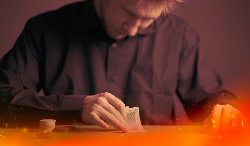 A poker player in a dark shirt lifting the corner of his cards while stacks of chips sit on the table.