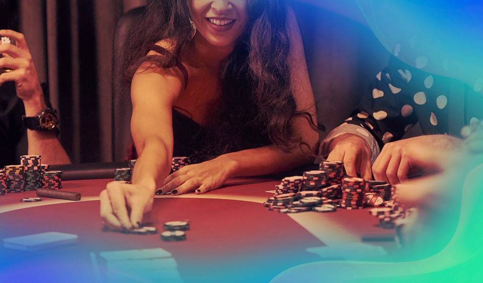 Close-up of a woman with long curly hair reaching for poker chips on a casino table, smiling confidently. Other players’ hands and stacks of chips are visible.