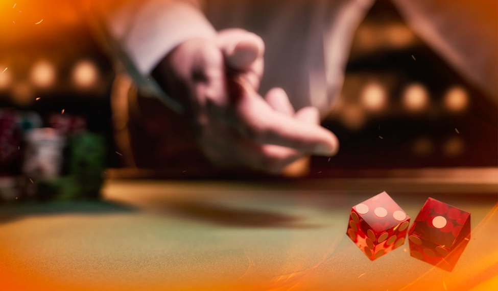 A hand rolls red dice across a green craps table in a dimly lit casino.