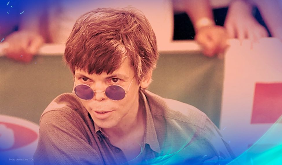 Stu Ungar at a poker table, wearing blue round sunglasses and focusing intently on the game with a crowd in the background.